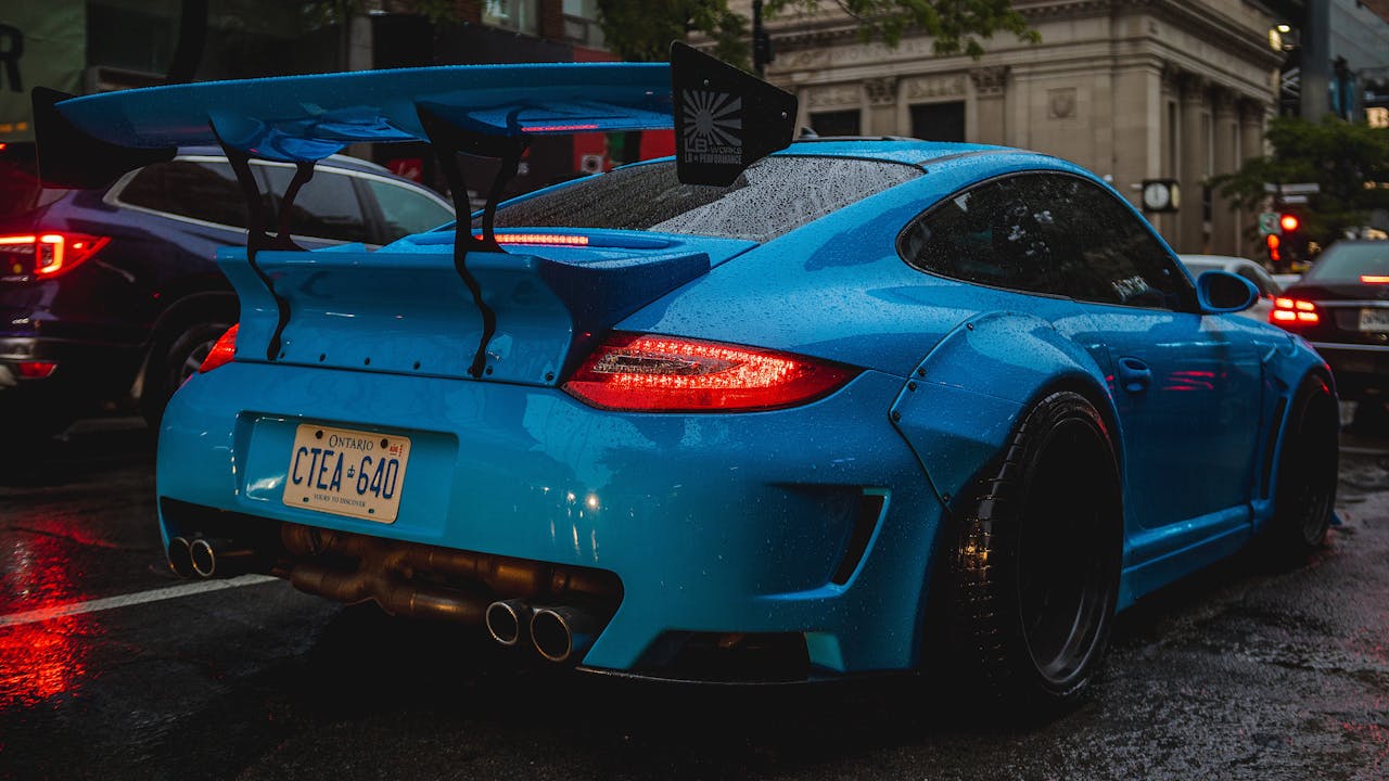 Dynamic blue sports car with large spoiler parked on a rainy city street, creating a dramatic urban ambiance.